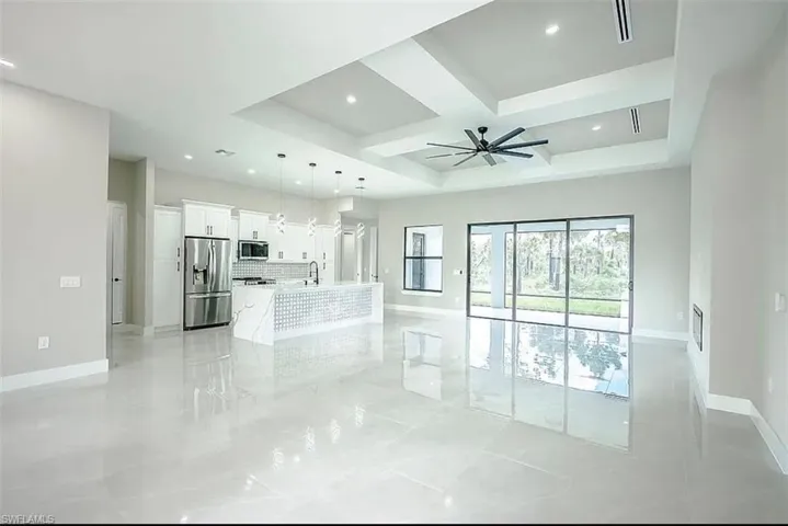 Unfurnished living room with sink, light tile patterned floors, coffered ceiling, ceiling fan, and a raised ceiling