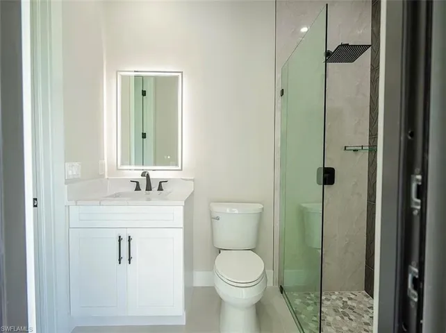Bathroom with tile patterned flooring, vanity, toilet, and tiled shower