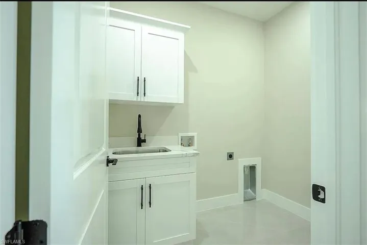 Washroom featuring light tile patterned flooring, hookup for an electric dryer, washer hookup, cabinets, and sink