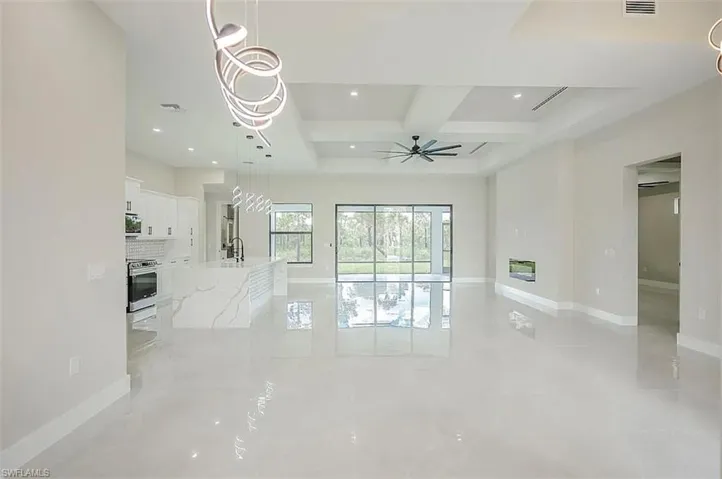 Unfurnished living room featuring a raised ceiling, coffered ceiling, sink, beamed ceiling, and ceiling fan with notable chandelier
