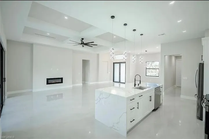 Kitchen with stainless steel appliances, white cabinetry, sink, light stone counters, and an island with sink