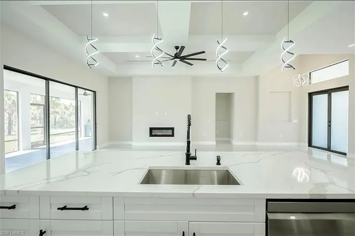 Kitchen featuring white cabinets, stainless steel dishwasher, light stone counters, and sink