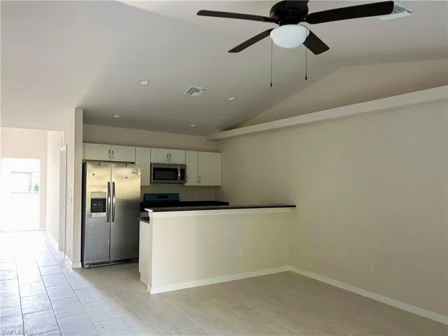Kitchen featuring white cabinets, stainless steel appliances, ceiling fan, and lofted ceiling