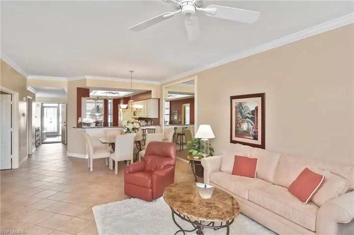 Living area with ornamental molding, light tile patterned floors, a chandelier, and ceiling fan
