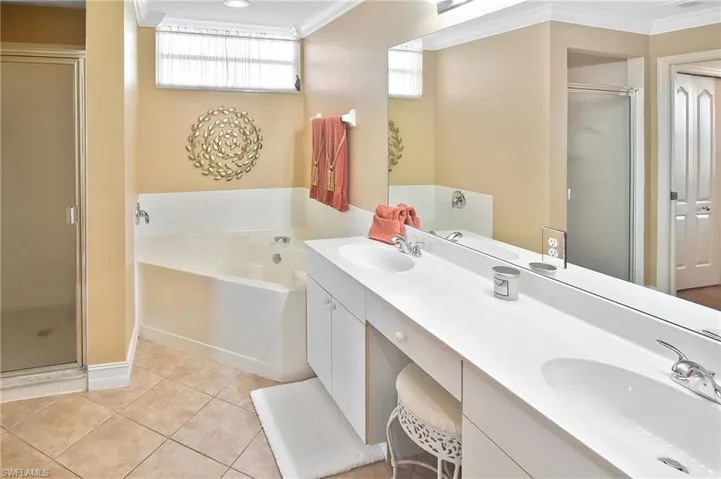 Bathroom featuring ornamental molding, a bath, a shower stall, double vanity, and light tile patterned flooring