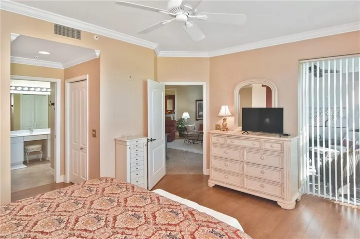 Bedroom featuring crown molding, light wood finished floors, a ceiling fan, and ensuite bath