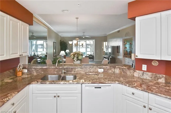 Kitchen featuring white cabinets, crown molding, white dishwasher, dark stone counters, and pendant lighting