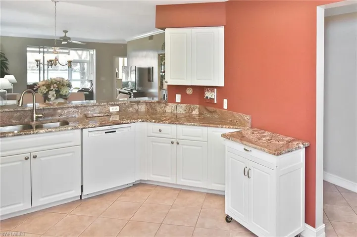Kitchen with white cabinets, dishwasher, light stone counters, light tile patterned floors, and hanging light fixtures