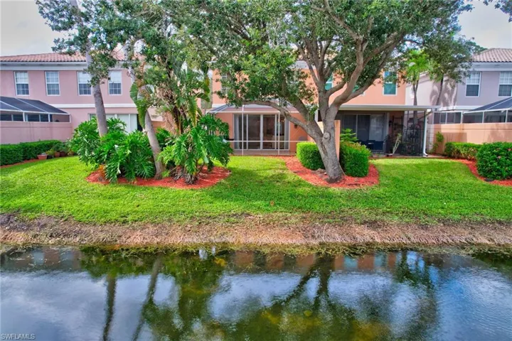 Back of house with a sunroom, a water view, and a lawn