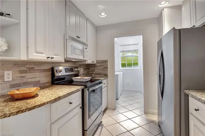 Kitchen featuring tasteful backsplash, light tile patterned flooring, light stone countertops, white cabinetry, and appliances with stainless steel finishes