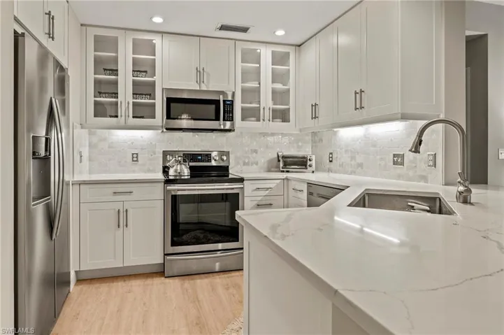 Kitchen with white cabinetry, light wood-type flooring, stainless steel appliances, decorative backsplash, and sink