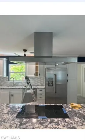 Kitchen featuring black electric stovetop, tasteful backsplash, high quality fridge, stone countertops, and white cabinetry