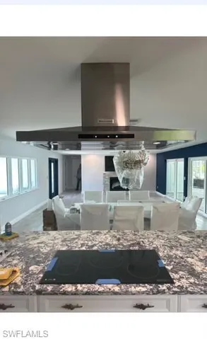 Kitchen featuring white cabinets, black electric stovetop, plenty of natural light, and wall chimney range hood