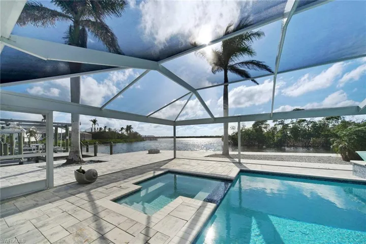 View of pool featuring a lanai, a patio area, a water view, and an in ground hot tub