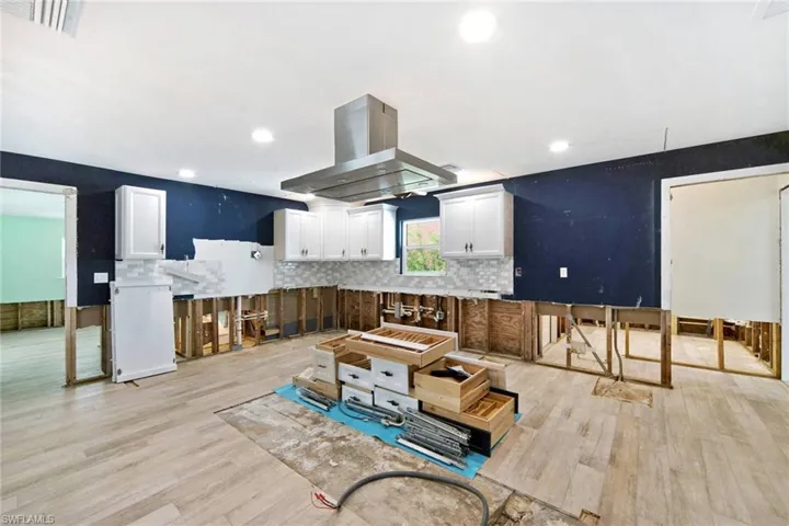 Kitchen featuring white cabinets, light wood-type flooring, tasteful backsplash, and island exhaust hood