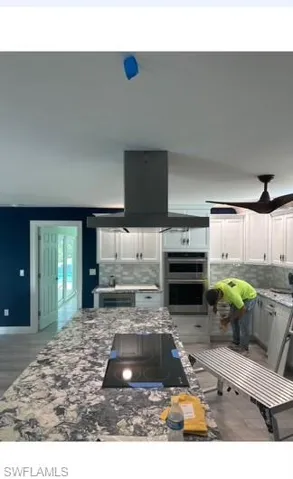 Kitchen with decorative backsplash, white cabinetry, ceiling fan, and light stone counters