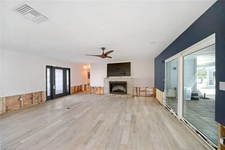 Unfurnished living room featuring plenty of natural light, a stone fireplace, wooden walls, and light hardwood / wood-style flooring