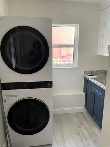 Clothes washing area with light hardwood / wood-style floors, cabinets, and stacked washer and clothes dryer