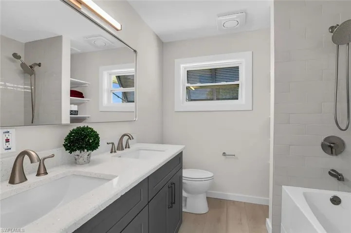Full bathroom with dual sinks, quartz counter and backsplash, tiled shower / over-sized bathtub combo