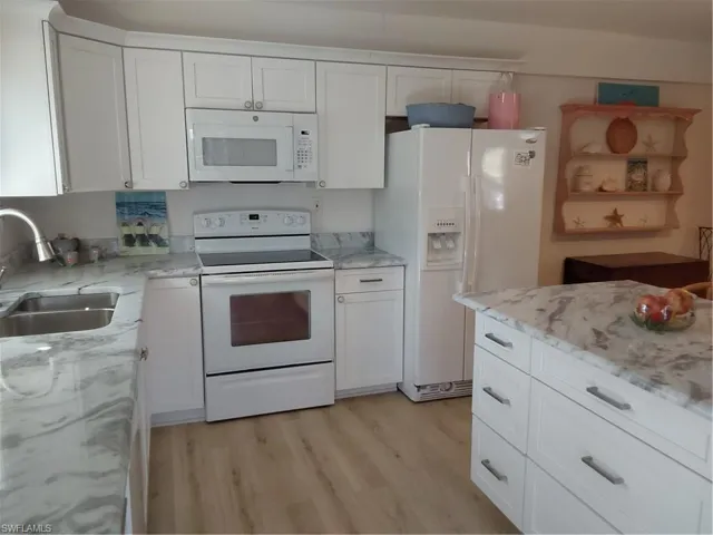 Kitchen featuring white appliances, light laminate / wood-style floors, white cabinetry, and beautiful granite countertops