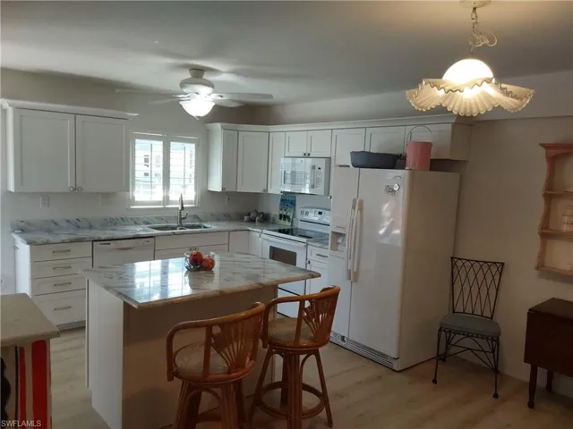 Kitchen featuring white appliances, sink, white cabinets, a center island, and hanging light fixtures