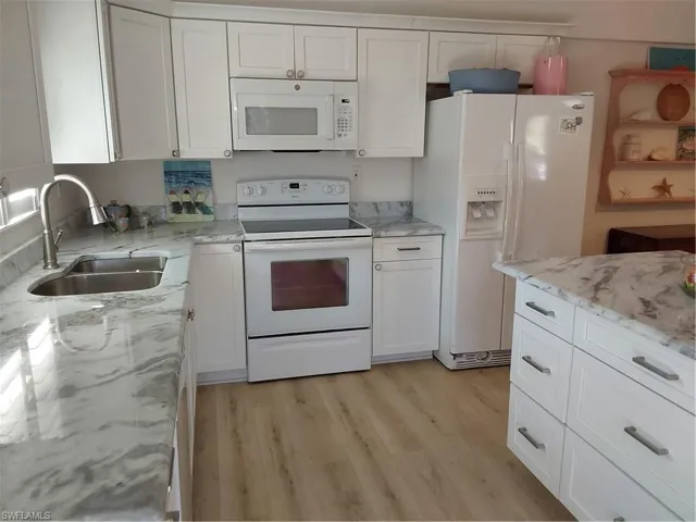 Kitchen featuring light stone counters, white appliances and white cabinets