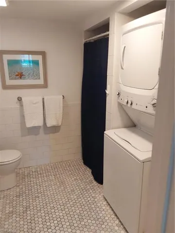 Laundry area featuring stacked washer and dryer, light tile patterned floors, and tile walls