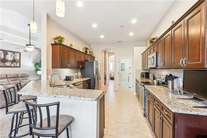 Kitchen featuring a peninsula, arched walkways, a breakfast bar, appliances with stainless steel finishes, and light stone counters