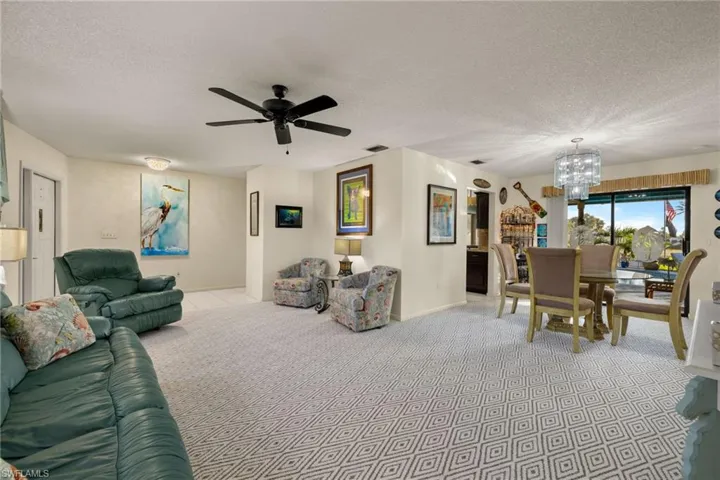 Carpeted living room with a textured ceiling and ceiling fan with notable chandelier
