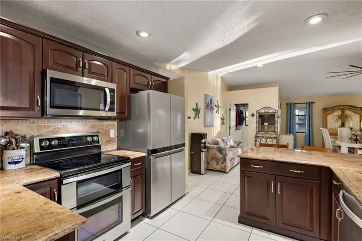 Kitchen featuring appliances with stainless steel finishes, tasteful backsplash, dark brown cabinets, a textured ceiling, and light tile patterned flooring