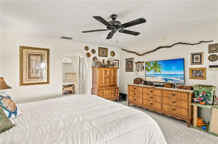 Carpeted bedroom with arched walkways, visible vents, a textured ceiling, and a ceiling fan