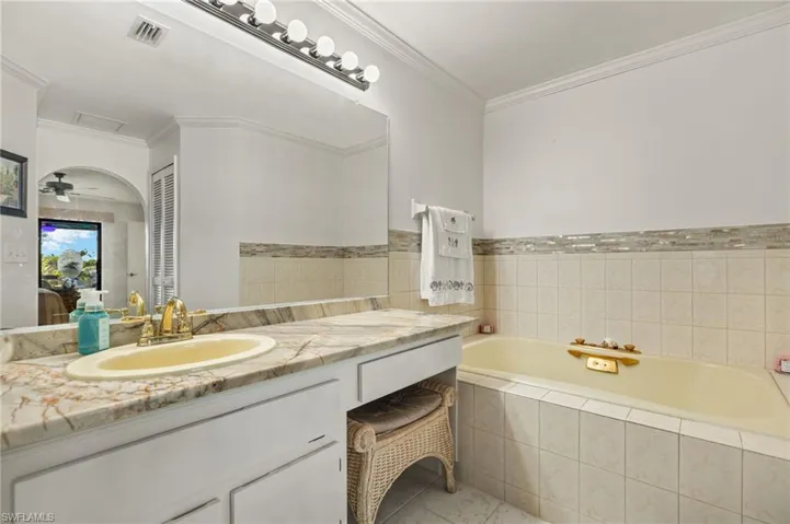 Full bathroom featuring visible vents, vanity, crown molding, and a garden tub