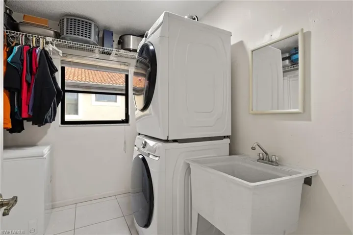 Laundry room with stacked washing maching and dryer, sink, and light tile patterned floors