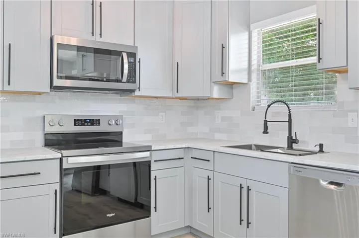 Modern kitchen featuring light gray cabinetry with black hardware, white quartz countertops, a white subway tile backsplash, and stainless steel appliances