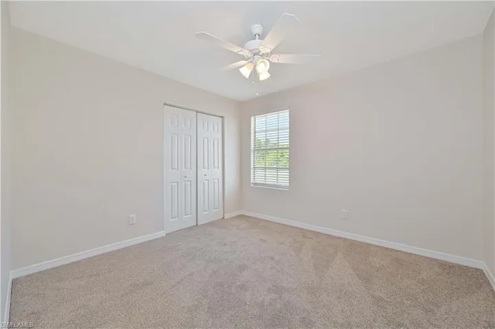 Carpeted room featuring a ceiling fan with integrated lighting, a window with horizontal blinds, and bi-fold closet doors