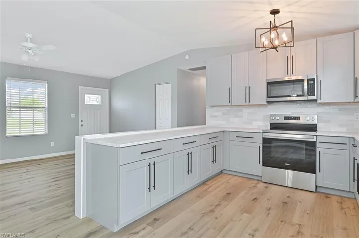 Modern kitchen featuring light gray cabinetry, stainless steel appliances, white subway tile backsplash, and light wood-finish flooring