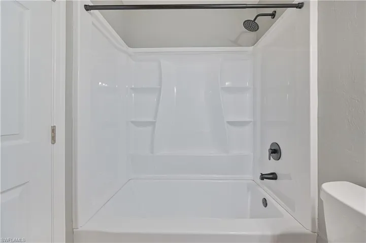 White bathtub and shower combination unit featuring integrated shelving, a matte black showerhead, and coordinating matte black tub filler and control