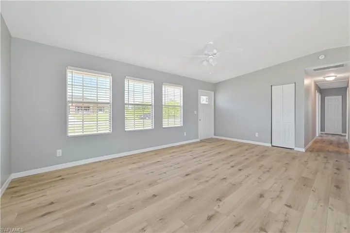 Spacious living area featuring light wood-finish flooring, three windows with blinds, and a white ceiling fan