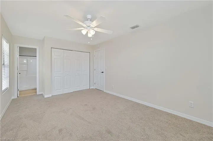 Carpeted room featuring a ceiling fan with light fixture, white bi-fold closet doors, and an open doorway to a bathroom with a white shower/tub combo