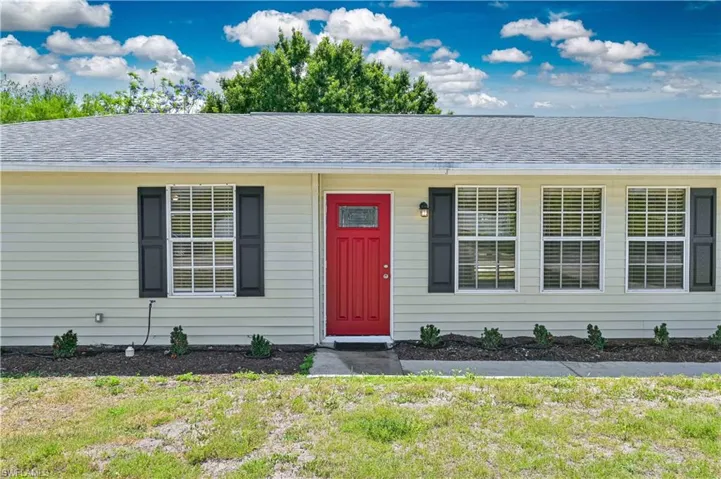 Front exterior featuring a vibrant red entry door with sidelight, light-colored horizontal siding, and a gray shingle roof