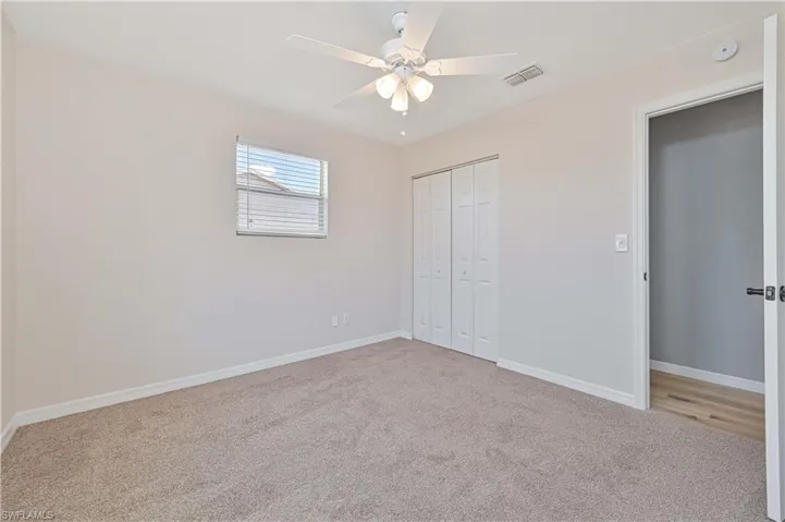 Neutral tone walls featuring carpet flooring, a window with blinds, bi-fold closet doors, and a ceiling fan with integrated lighting