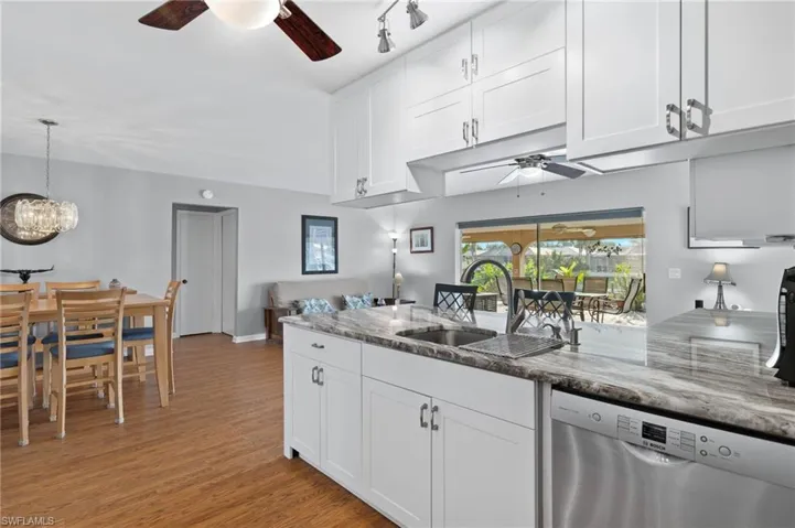 Kitchen with ceiling fan, dishwasher, light wood-style floors, white cabinets, and light stone countertops