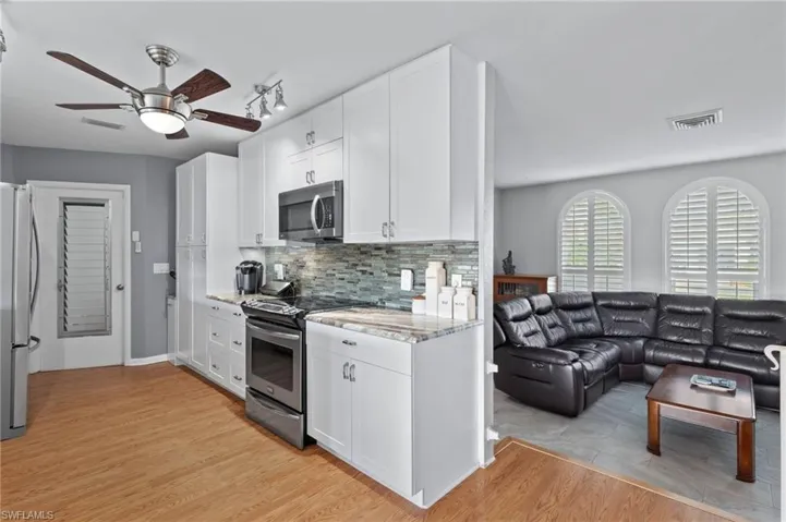 Kitchen featuring appliances with stainless steel finishes, white cabinetry, a ceiling fan, backsplash, and open floor plan