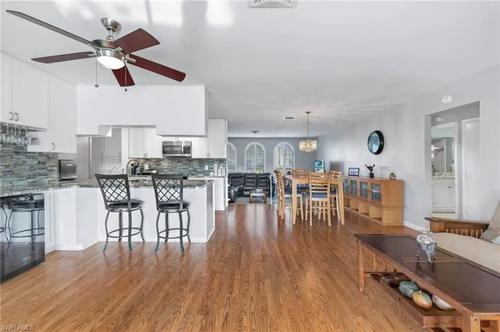 Kitchen with decorative backsplash, white cabinetry, wood finished floors, a peninsula, and a breakfast bar area