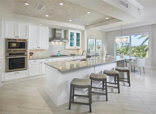Kitchen with a tray ceiling, backsplash, appliances with stainless steel finishes, a breakfast bar, and light stone countertops