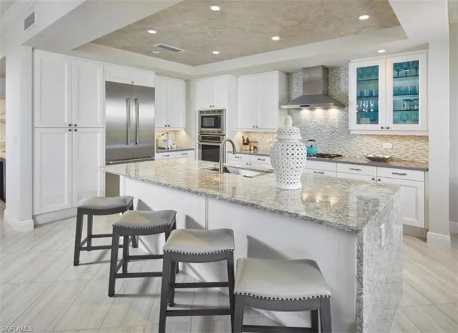 Kitchen featuring a raised ceiling, light stone countertops, white cabinets, a kitchen breakfast bar, and recessed lighting
