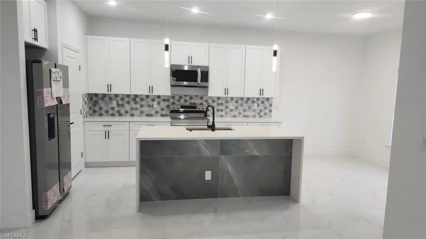 Kitchen with tasteful backsplash, sink, white cabinets, and appliances with stainless steel finishes