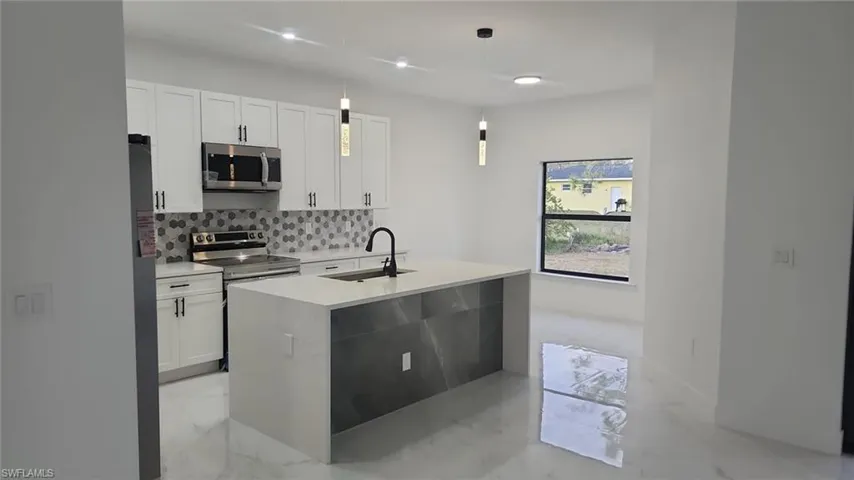 Kitchen featuring pendant lighting, sink, white cabinetry, a kitchen island with sink, and stainless steel appliances