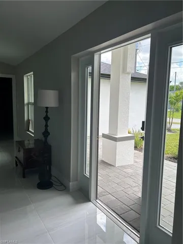 White tile flooring throughout, leading to a front entry with glass panel doors and an exterior paver patio