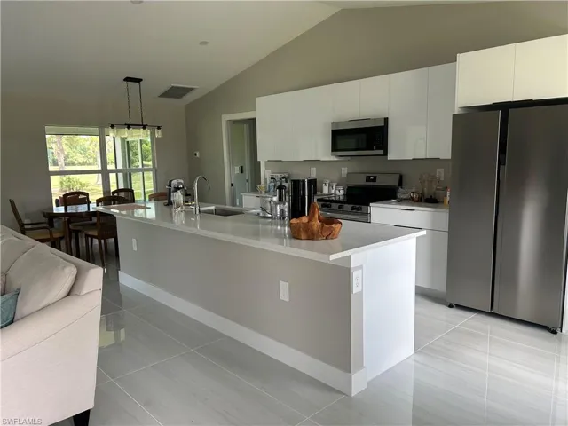 Modern kitchen featuring white cabinetry, stainless steel appliances, a center island with sink, and light-toned tile flooring